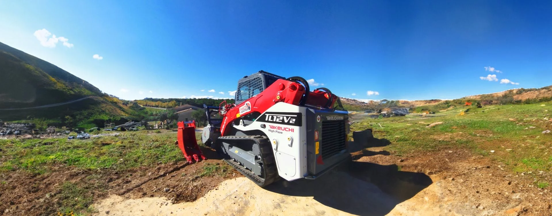 Chargeur compact de la marque Takeuchi, modèle TL12V2 entouré de montagne et de verdure