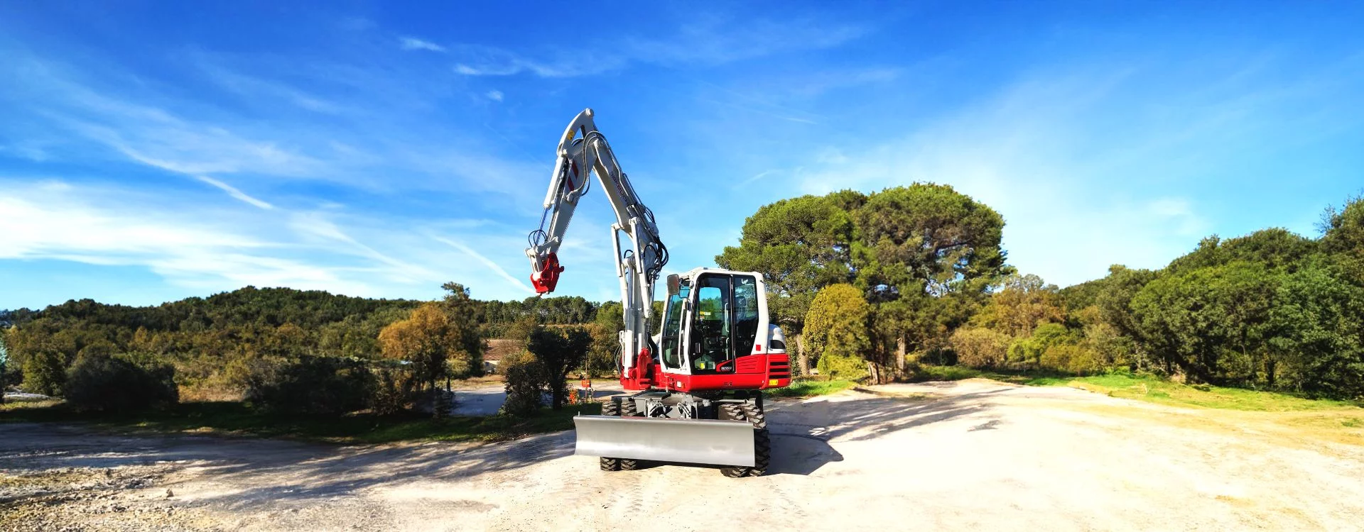 Pelle sur pneus TB395 W de chez Takeuchi, sur terrain plat et entouré d'arbres